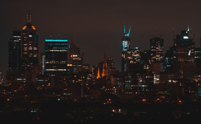 Modern city skyline at dusk with abstract, glowing blue lines representing data and AI analysis overlaid on the buildings.