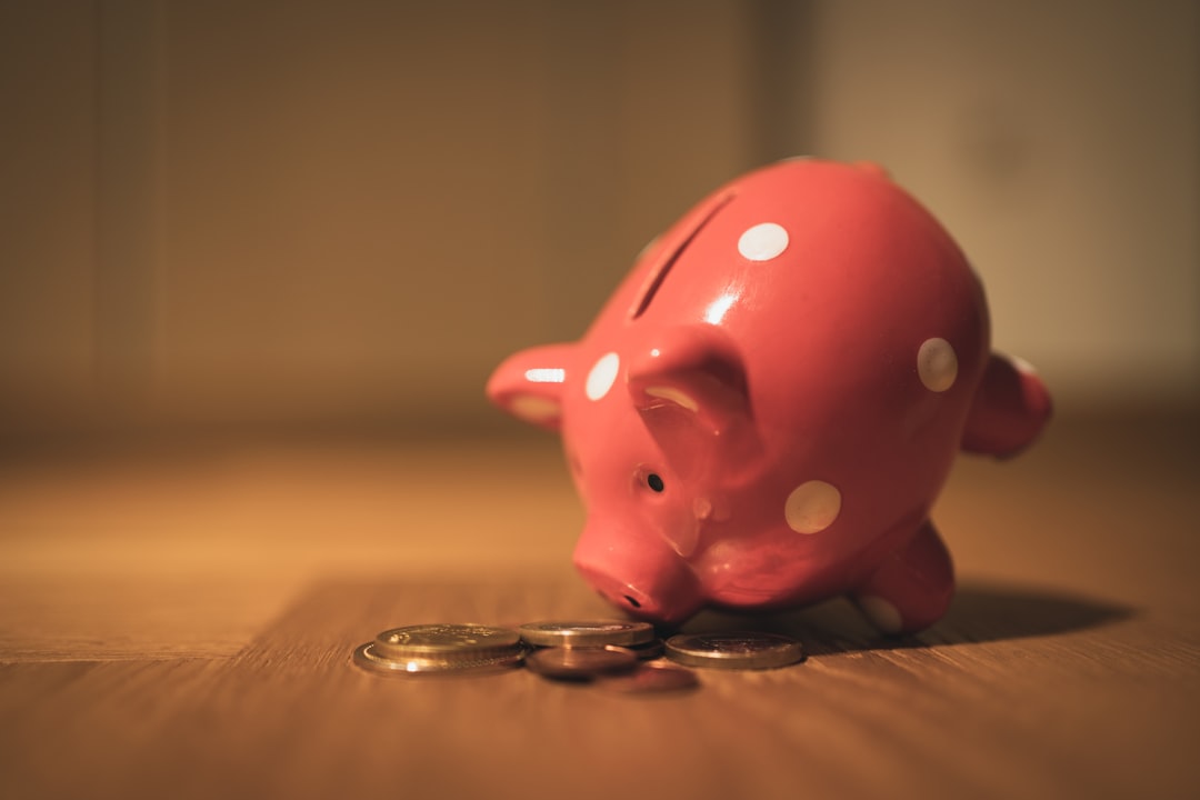 A hand drops a coin into a white, house-shaped piggy bank on a minimalist background, representing the significant savings from low-commission real estate.